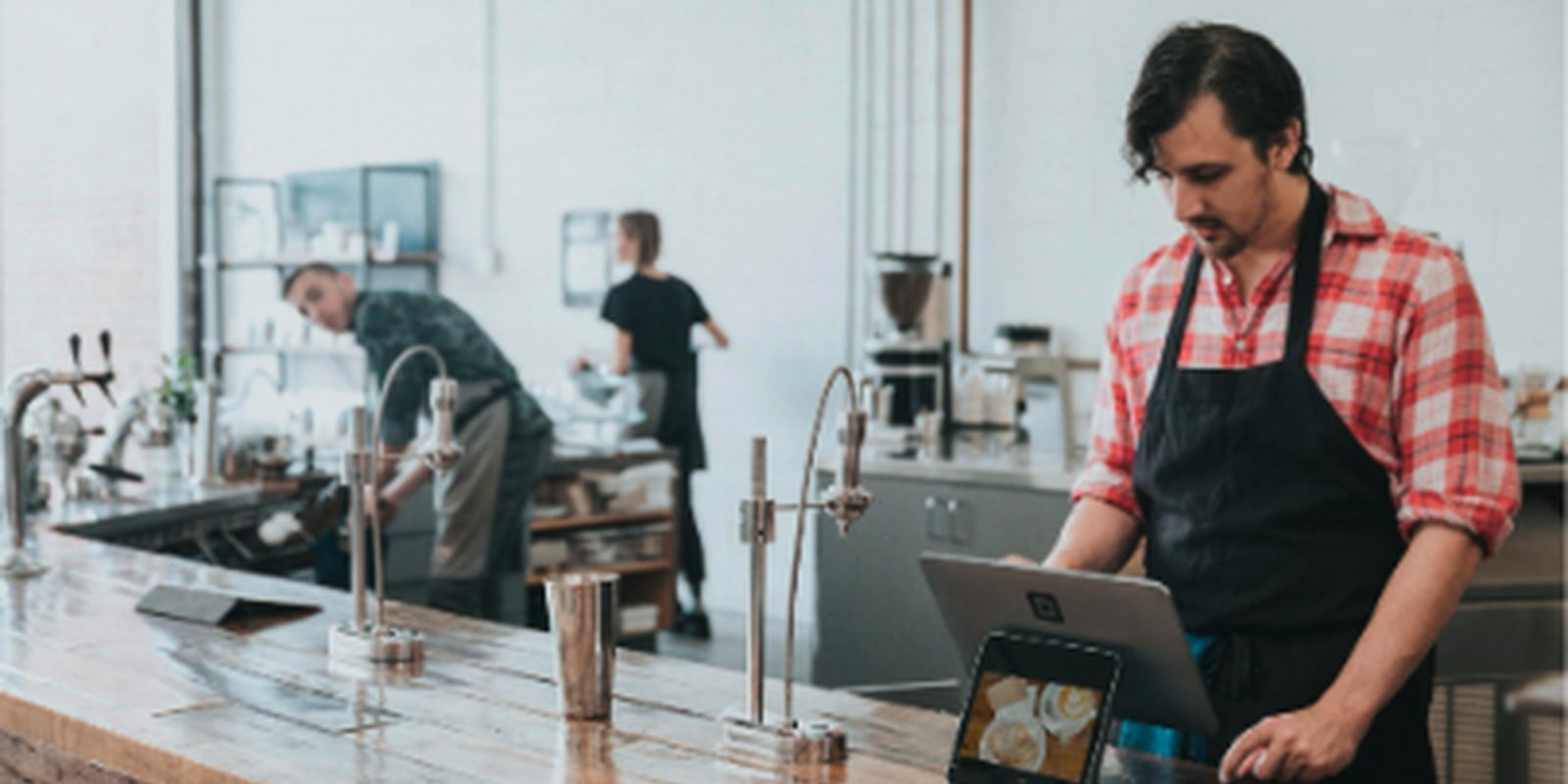Barista using a POS tablet behind the ordering counter in a bright specialty coffee shop.